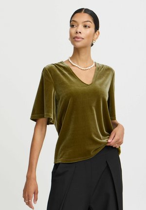 Olijf groene fluwelen T-shirt met een V-hals, korte mouwen en een relaxed fit, gecombineerd met zwarte broek. Glad textuur en subtiele glans.