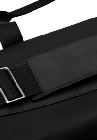 Černá messenger taška s hladkým matným povrchem, která má textilní popruh a stříbrnou kovovou sponu. Diskrétní detail loga s ražením.