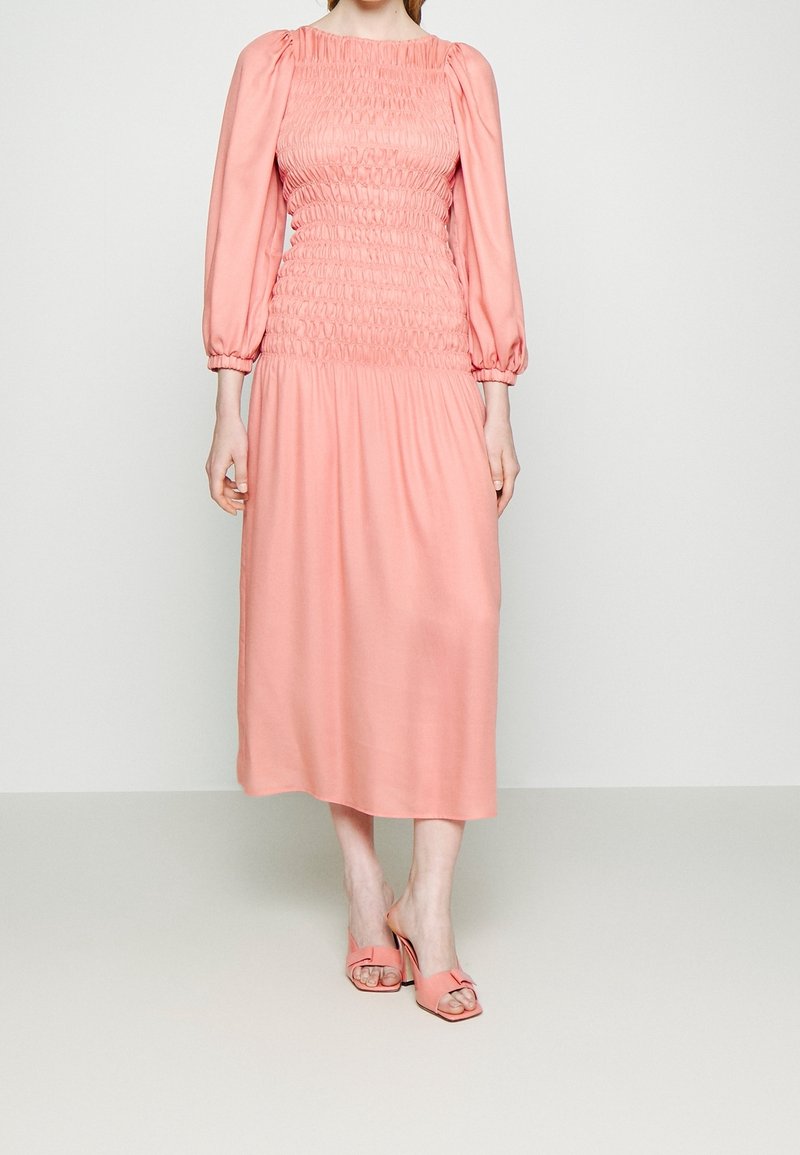 Vaaleanpunainen midi-mekko smokkibodalla, puffihihnat ja leviävä helma. Yhdistetty vaaleanpunaisiin korkokenkiin, joissa on nauhatyyppinen yksityiskohta.