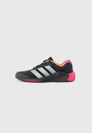 Schwarzer Sportschuh mit weißen Streifen, pinker Ferse und orange-violettem Innenfutter, seitlich auf grauem Hintergrund dargestellt.