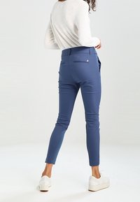 Námořnické modré přiléhavé kalhoty s elegantním designem a bočními kapsami. Vyrobené z hladkého materiálu, s detailem zipu na zadní straně a délkou ke kotníkům.