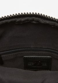 Interno di una borsa nera con chiusura a zip, caratterizzato da una superficie liscia e un’etichetta in pelle. La fodera è di un tessuto scuro con bordo rigato.