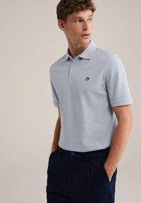 Cămașă polo bleu deschis, din bumbac, cu un guler clasic și un mic logo brodat negru pe pieptul stâng. Asortată cu pantaloni negri închis.