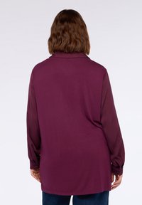 Blusa a maniche lunghe color mirtillo con collo, vestibilità ampia e polsini abbottonati. Il tessuto liscio e l'orlo dritto definiscono il suo design.