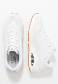 Baskets de sport blanches avec un design perforé, des lacets et une semelle intérieure en mousse à mémoire de forme. Semelle en caoutchouc avec une fonction d'amortissement par air sur le côté.