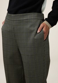 Pantaloni a fantasia neri e grigi con un tessuto strutturato, dotati di tasche laterali e design a gamba dritta. La vita è liscia e aderente.