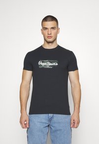 Camiseta negra de algodón con mangas cortas y escote redondo. Presenta un logo de "Pepe Jeans London" en blanco sobre una franja verde texturizada.