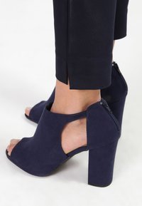 Mörkblå mocka öppna tå-höga klackskor med en tjock klack och sidouttag, med en dragkedjestängning bak.