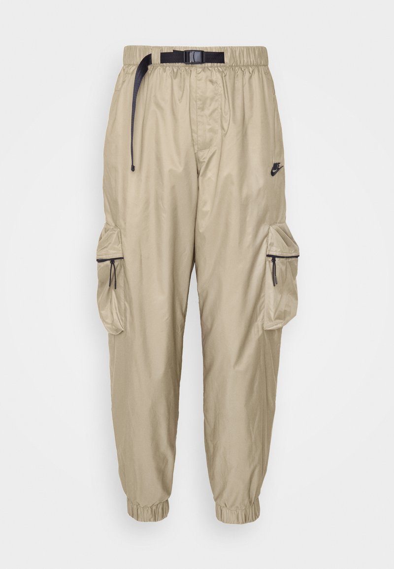 Pantalons cargo en nylon beige avec une taille élastique, une ceinture ajustable et deux poches latérales avec fermetures éclair. Comprend des poignets élastiques.