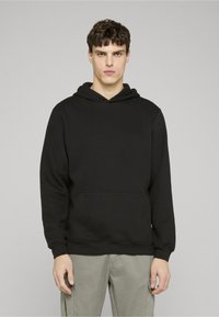 Crna dukserica s kapuljačom s vezicama, prednjim džepom na preklop, gumenim manžetama i rubom. Mekani materijal glatke teksture, jednostavan dizajn.