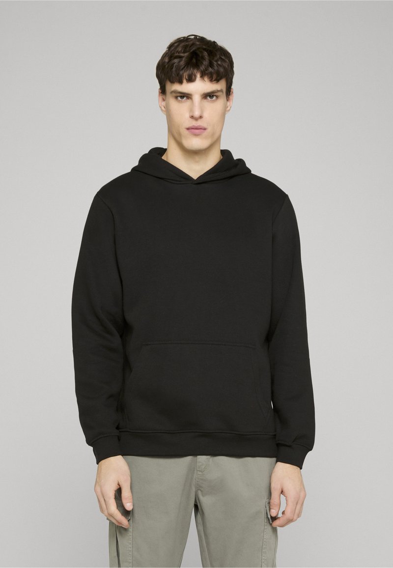 Crna dukserica s kapuljačom s vezicama, prednjim džepom na preklop, gumenim manžetama i rubom. Mekani materijal glatke teksture, jednostavan dizajn.