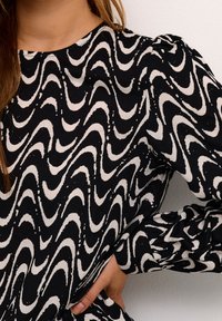 Czarny i biały top z długim rękawem z falistym wzorem. Materiał wydaje się gładki z delikatnym połyskiem; detal w postaci bufiastego rękawa podkreśla design.