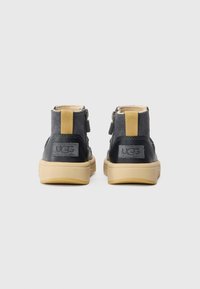 Vue arrière de bottines noires en suède avec des accents jaunes et une semelle en caoutchouc, présentant une fermeture éclair et un logo UGG sur le talon.