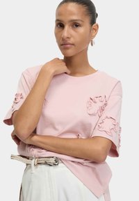 Ljusrosa bomulls-t-shirt med volangdetaljer på ärmarna och bröstet, rund halsringning och avslappnad passform. Matcher med ett vävt bälte.