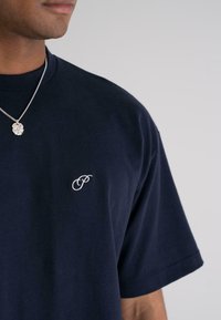 Navy blue cotton t-shirt with a slightly loose fit, featuring a small white embroidered logo on the left chest and a crew neck design.