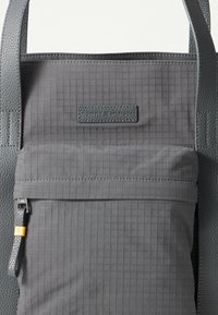 Sac fourre-tout texturé gris avec poche zippée à l'avant, dotée d'une languette en cuir et d'une étiquette de marque en cuir cousue.