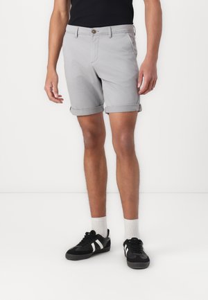 Gray cotton shorts with rolled cuffs, a front button closure, and side pockets, paired with black sneakers and white ankle socks.