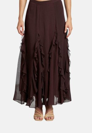 Falda maxi marrón, fluida, con capas rizadas y acentos transparentes. Cintura elástica. Combinada con tacones de tiras beige.