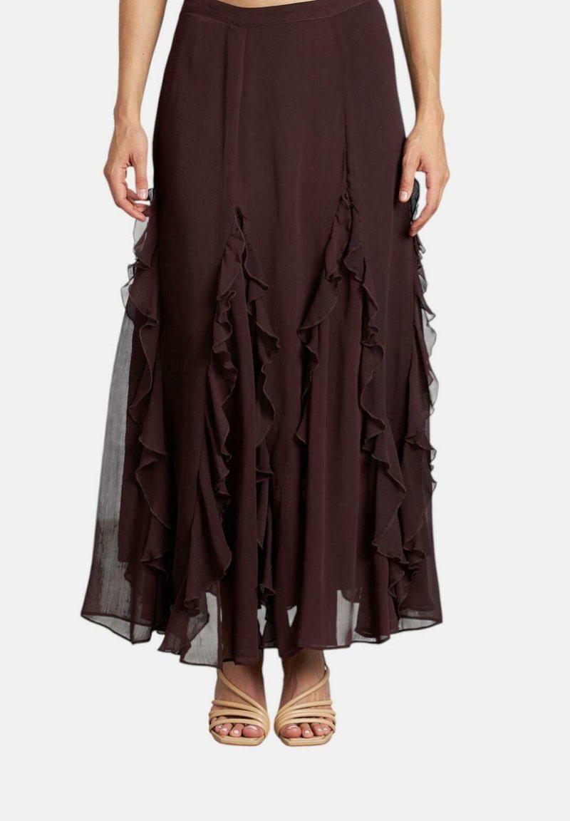 Gonna maxi marrone fluida con strati arricciati e dettagli trasparenti. Vita elastica. Abbinata a tacchi beige con cinturini.
