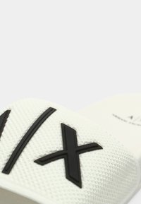 Sandália branca de cunha com parte superior em tecido texturizado e detalhes em borracha preta num design geométrico. Sola plana e estilo com dedo aberto.