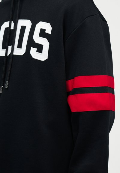 Svart hettejakke med hvite GCDS-bokstaver på brystet, svarte snorer og to horisontale røde striper på ermet.