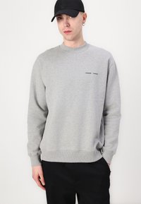 Gray sweatshirt with crew neck, ribbed cuffs and hem, featuring a small black printed logo on the chest. Fabric appears soft and smooth.