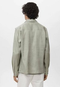 Svetlo zelena majica z dolgimi rokavi iz mehkega, teksturiranega materiala. Ima ovratnik, gumbne manšete in prilegajoč kroj, z enostavno zasnovo na hrbtni strani.