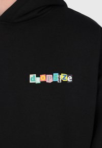 Haut à capuche noir avec des lettres colorées dans le style des lettres de rançon écrivant "drop size" centrées sur la poitrine.