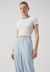Witte, geknipte geribbelde t-shirt met korte mouwen, gedragen met lichtblauwe, losse broek met een elastische tailleband.