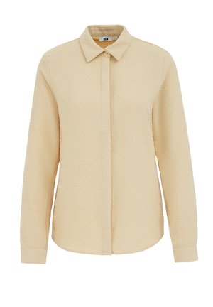 Hosszú ujjú, világos bézs színű galléros ing, amely texturált szövettel rendelkezik, apró kiemelkedő pöttyökkel, elöl gombos záródással és íves szegéllyel.