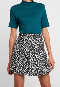 Teal kortærmet top med høj hals, parret med en sort nederdel med hvidt leopardmønster. Glat materiale, tætsiddende design, over-knee længde.