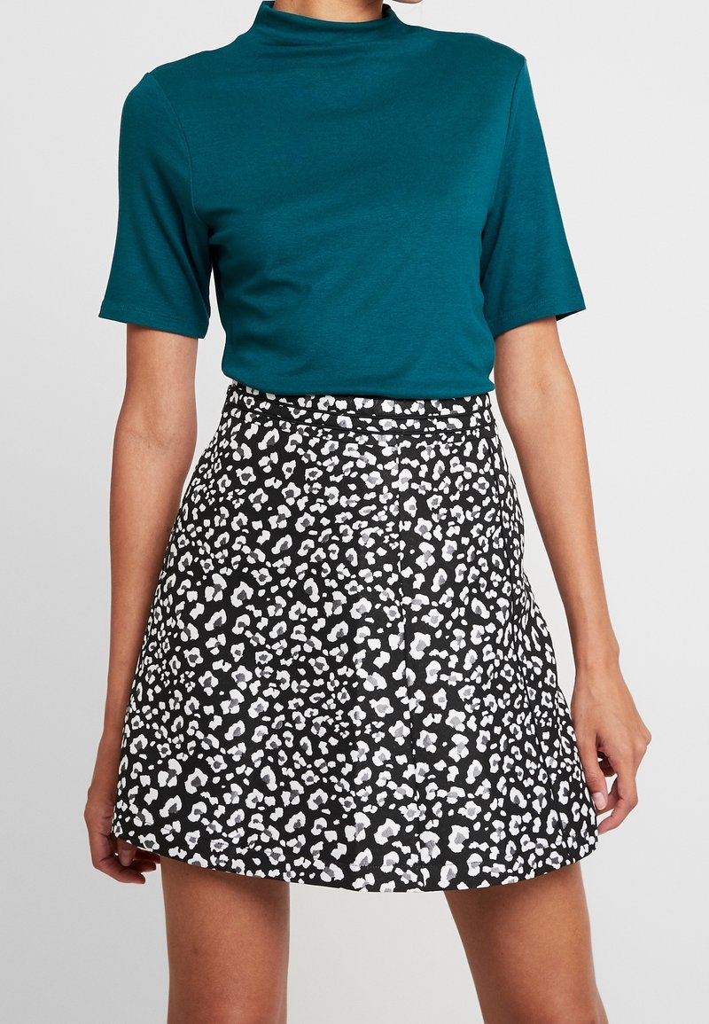 Teal kortærmet top med høj hals, parret med en sort nederdel med hvidt leopardmønster. Glat materiale, tætsiddende design, over-knee længde.