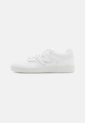 Witte lage sneaker met geperforeerde neus, vetersluiting en een grote reliëf letter "N" aan de zijkant.