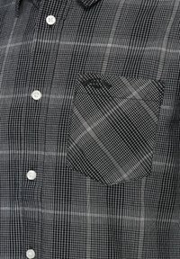 Černobílá kostkovaná košile na knoflíky s náprsní kapsou s diagonální mřížkovaným vzorem a bílými knoflíky.