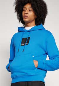Blauwe hoodie van een katoenmix met een voorzak, trekkoordkap en zwart vierkant logo. Strakke textuur, ribgebreide manchetten en zoom.