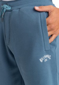 Modré teplákové kalhoty z měkké tkaniny mají žebrovaný pas, šňůrku na stažení, boční kapsy a vyšívané logo na stehně.