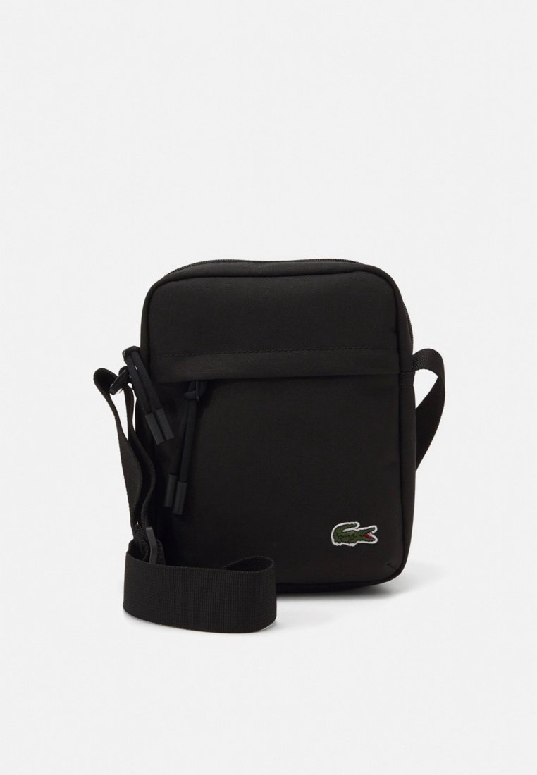 Sac bandoulière noir en tissu résistant, doté d'une texture lisse, d'une sangle réglable et d'un petit logo crocodile brodé.