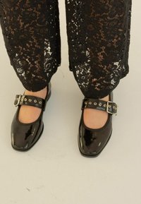 Chaussures Mary Jane noires en vernis avec un bout carré, décorées d'une large lanière ornée d'oeillets en argent et d'une boucle métallique.