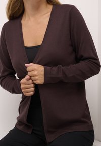 Cardigan léger marron avec un col en V profond et des manches longues, présentant un design minimaliste et une finition légèrement texturée.