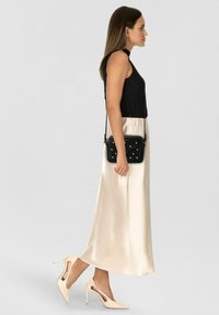 Top nero senza maniche, gonna maxi in satin color crema, scarpe con tacco alto color crema con ritagli, borsa a tracolla nera con dettagli di perle.