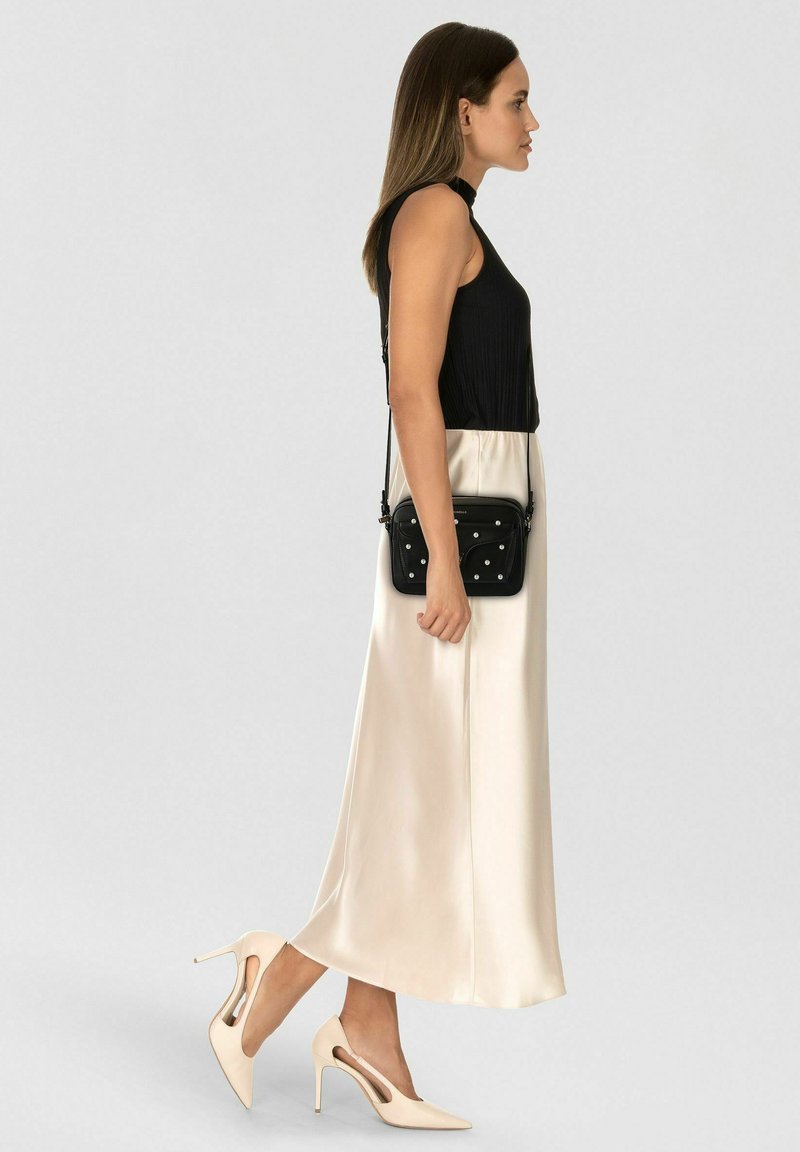 Top nero senza maniche, gonna maxi in satin color crema, scarpe con tacco alto color crema con ritagli, borsa a tracolla nera con dettagli di perle.