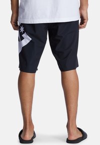 Schwarze Shorts aus leichtem Material mit einem großen weißen grafischen Design auf der linken Seite. Sie haben eine lockere Passform und einen mittellangen Schnitt.