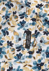 Bloemenpatroon stof met blauwe, beige en zwarte bladeren en bloemen, met een zwart etiket met de tekst "Elke stap een nieuwe reis."