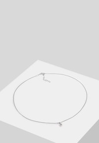 Collier en chaîne argentée au design élancé, avec un petit charme circulaire. La chaîne est lisse, dotée d'un fermoir en homard et d'une chaîne d'extension.