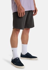 Grijze sportshorts met een elastische tailleband, gecombineerd met witte crew-sokken en marineblauwe sneakers met een gestructureerde bovenkant en witte zool.