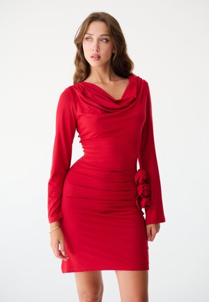 Abito lungo rosso a maniche lunghe con scollatura drappeggiata e silhouette aderente. Presenta una texture gathered e accenti di rose tridimensionali sui fianchi.