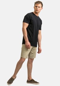 Maglietta nera a maniche corte, vestibilità rilassata, abbinata a pantaloni corti beige. Calzature: sneakers casual marroni. Linee semplici e pulite, senza motivi.