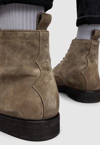 Stivaletti alla caviglia in suede beige con una finitura strutturata, caratterizzati da un sottile design a ondulazione sul tallone e una suola in legno scuro.