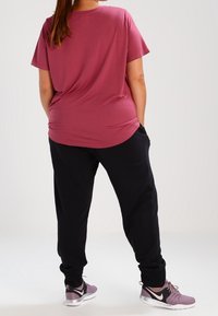 Bordový tričko s krátkým rukávem a kulatým výstřihem v kombinaci s černými tepláky. Obuv: fialové sportovní boty s bílými akcenty.