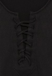 Černá žebrovaná látka s výstřihem do V a šněrovacím detailem na předním středu. Měkčí textura s kontrastní pevným panelem pod ním.